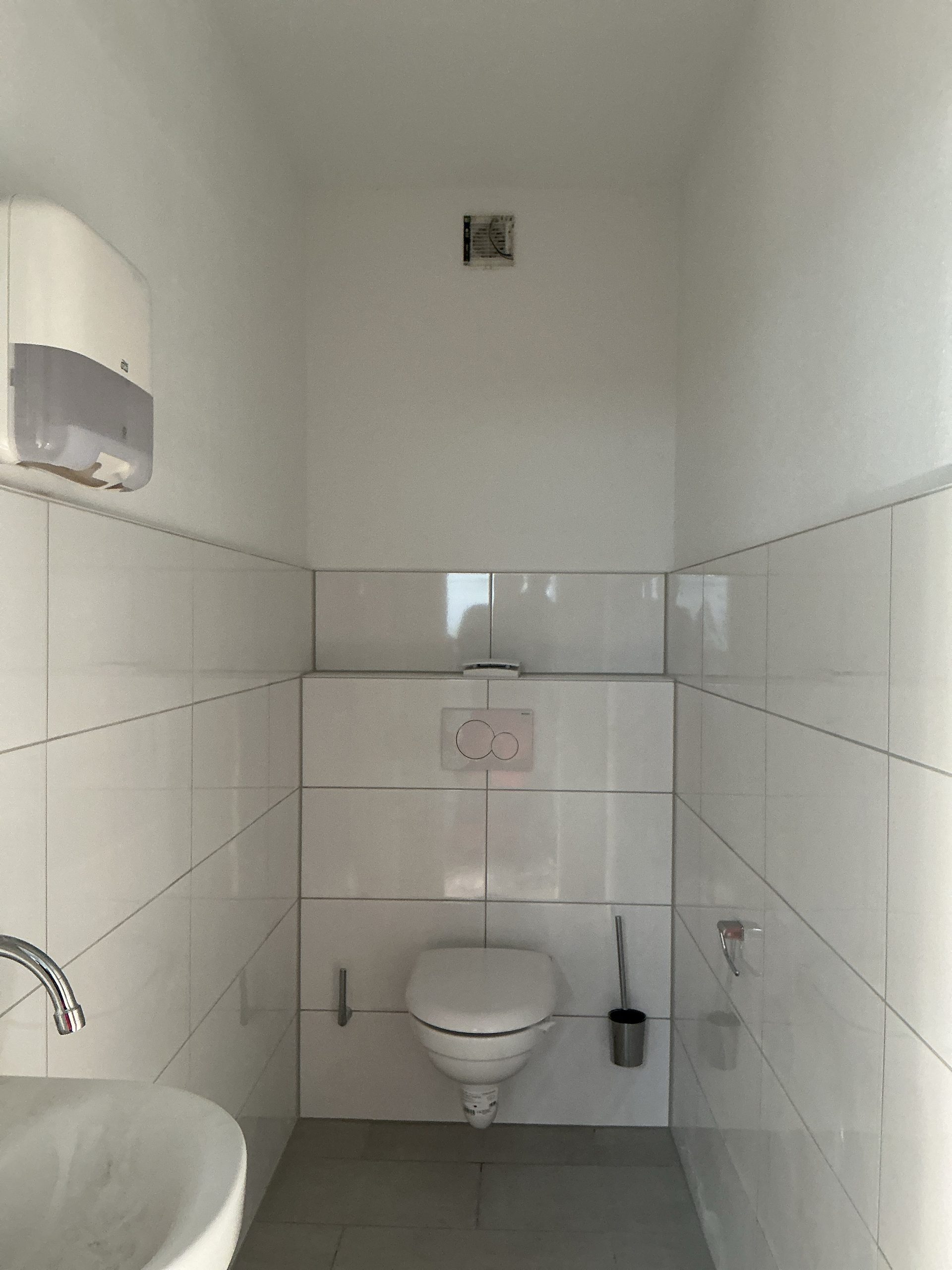 Projekt B. &ndash; gewerbliche Kundentoilette mit wandh&auml;ngendem WC, wei&szlig;en Fliesen und Papierhandtuchspender